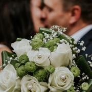 A married couple kissing behind a wedding bouquet. Credit: Canva